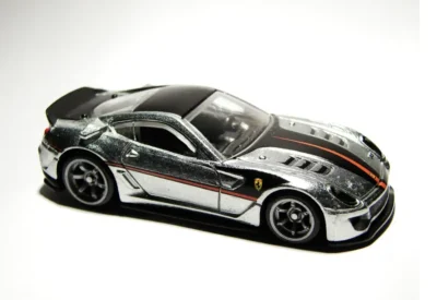 Modelo de carro esportivo em escala, com detalhes refletivos na pintura prateada, acessórios em preto, decorado com faixa laranja, ideal para colecionadores de carros.