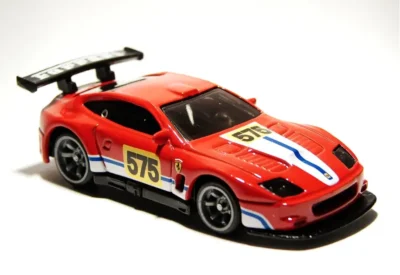Carrinho de corrida em miniatura vermelho com decalques azul e branco, número 575 e asa traseira, ideal para colecionadores e fãs de automobilismo.
