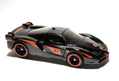 Modelo de carro esportivo em escala, com detalhes refletivos na pintura prateada, acessórios em preto, decorado com faixa laranja, ideal para colecionadores de carros.